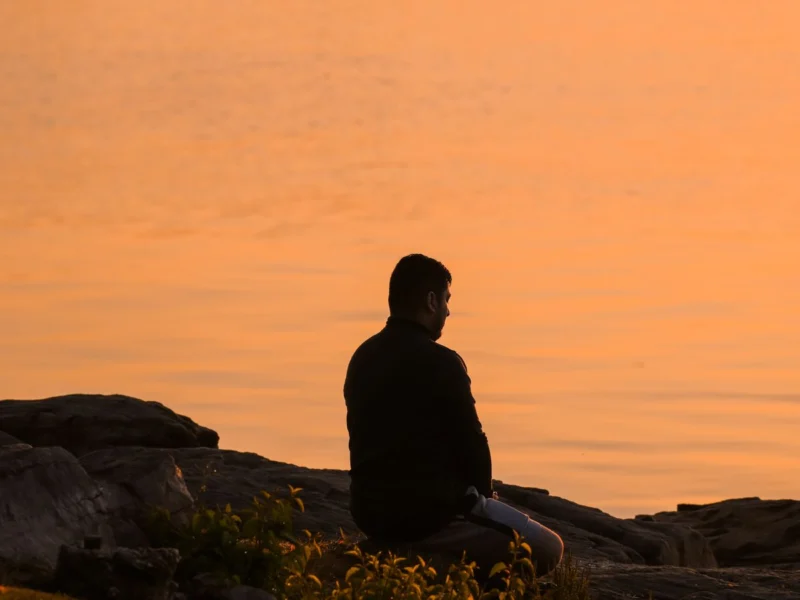 Person sitting on rocks by the water at sunrise