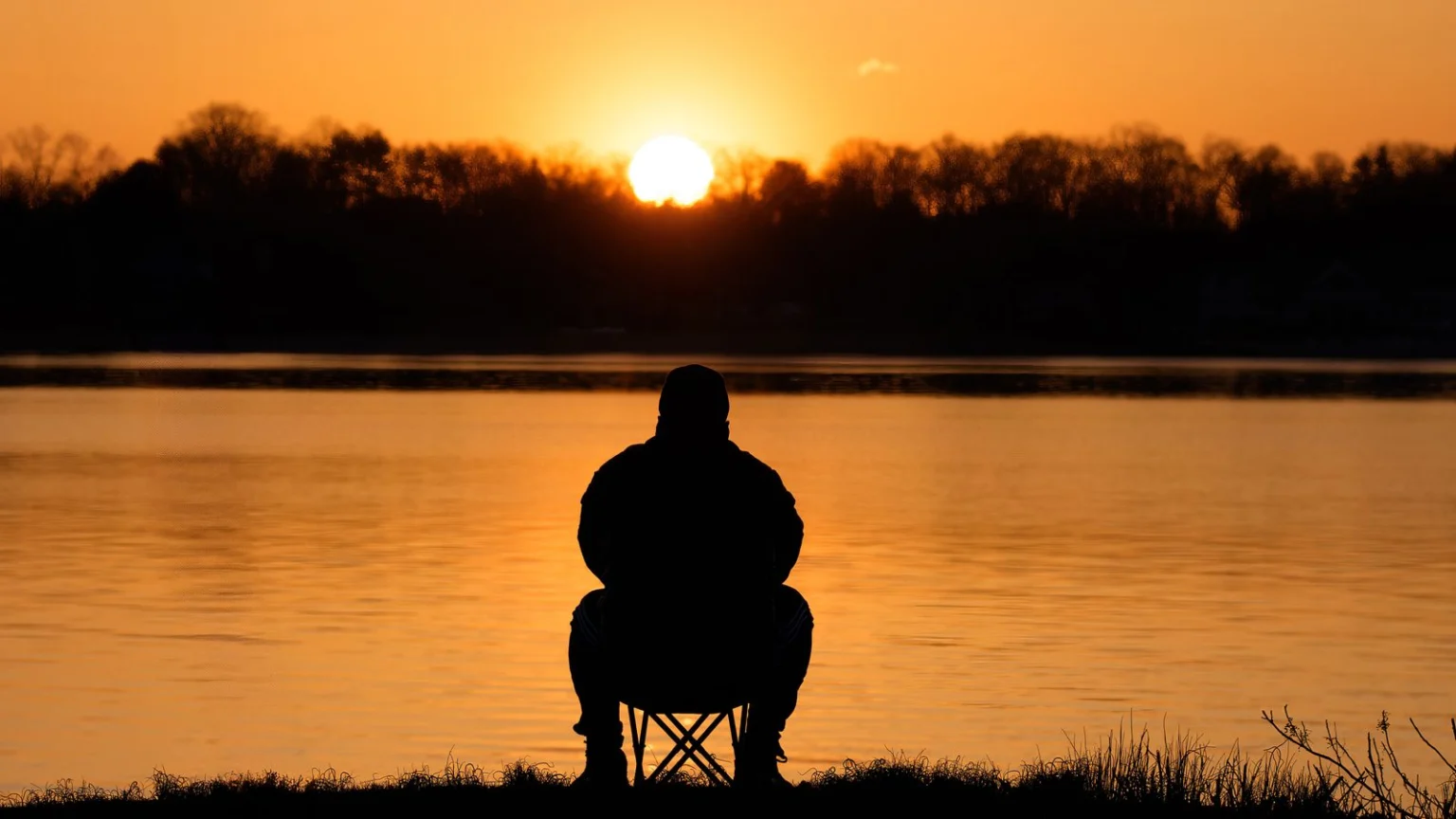 Silhouette of a person sitting quietly by the water at sunrise