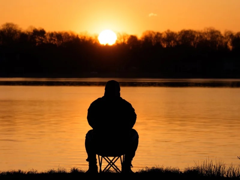 Silhouette of a person sitting quietly by the water at sunrise