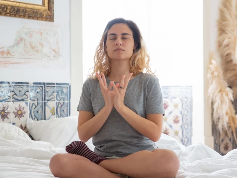 Woman meditating on her bed in soft morning light