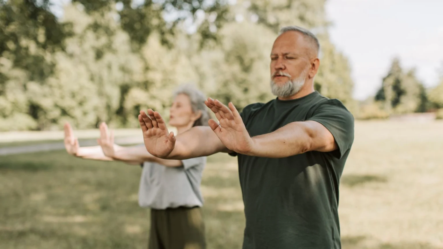 Older couple doing a gentle arm-raising exercise in a park