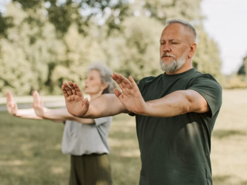 Older couple doing a gentle arm-raising exercise in a park