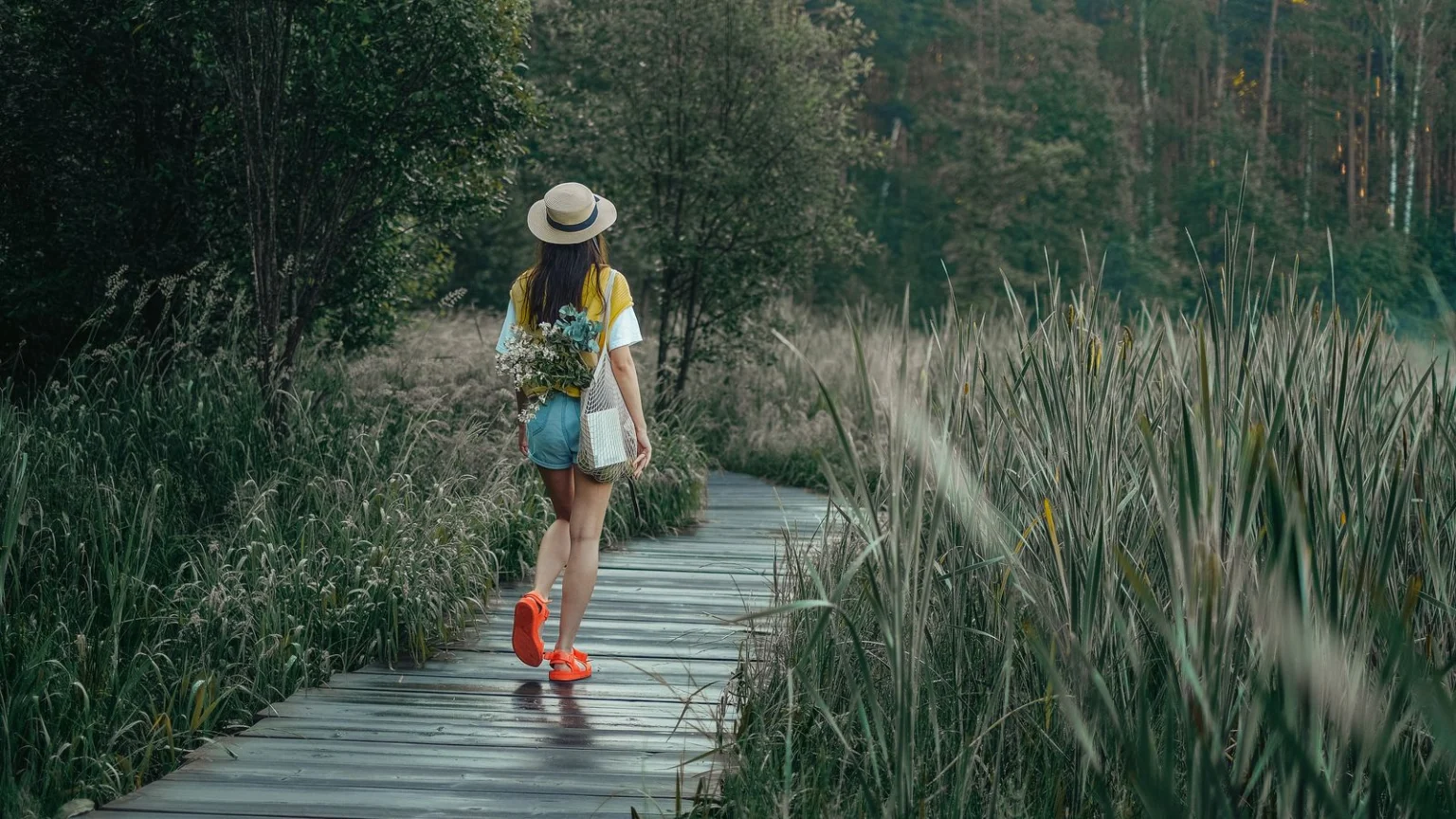 Woman in a sun hat walking along a wooden boardwalk